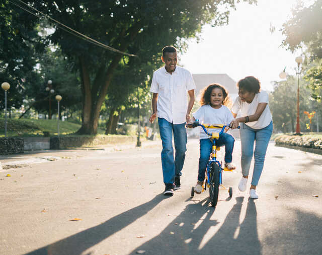 Parents teaching daughter how to ride her bike. 
