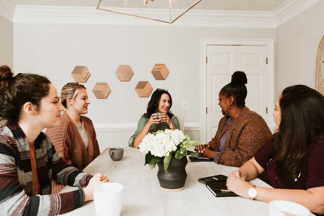 a group of women talking and drinking coffee around a table